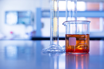 Wall Mural - glass beaker with orange solution and cylinder in blue chemistry laboratory background