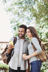 Beautiful happy couple using smartphone. Young joyful smiling woman and man looking at mobile phone in a city. Technology, travel, students concept