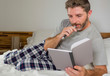 © TheVisualsYouNeed - lifestyle portrait of young attractive and relaxed man at home lying comfortable on bed taking notes with pen in notepad writing on his diary or agenda wearing  pajamas