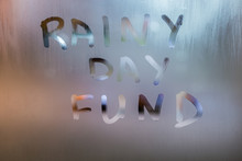 Words RAINY DAY FUND Written By Hand On Wet Glass At Morning With Blurry Street Light Background