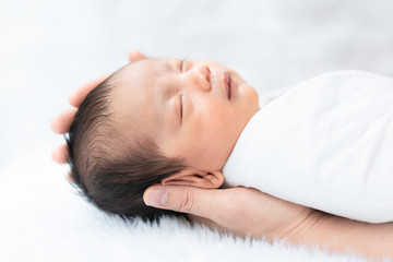 A cute sleeping newborn baby boy gentle holding by his parent's hand, concept of care and support of parent to their infant with love in family lifestyle.