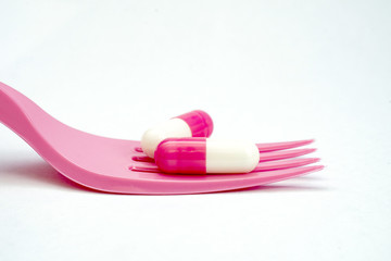 two pink white capsules on a disposable fork on white