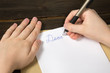 © somemeans - Children's hands writing a letter to Santa. Wooden background. Close-up