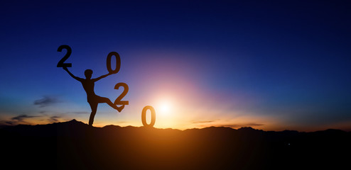 Silhouette of man doing walking on hill and 2020 years while celebrating new year at sunset background.