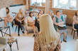 Rear view of female speaker giving a talk at business meeting. Participant in audience are out of focus.