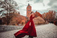 Beautiful Girl In A Burgundy Red Dress Walking Near  Old Castle On A Background Of Autumn Grape Leaves In The Park, October. Radomyshl