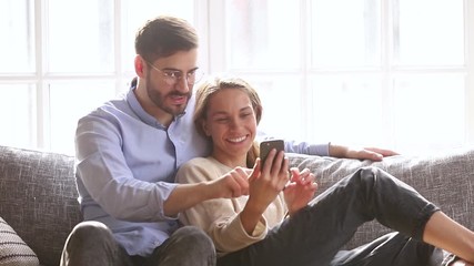 Canvas Print - Happy couple talk laugh looking at smartphone sit on couch