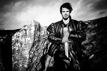 Wall Mural - Portrait of handsome knight standing next to rock holding sword and looking at camera