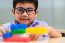 A Cute Asian Elementary School Boy Student Wearing Glass And White Uniform Is Sitting And Playing Creative Toys By Connecting Each Parts To Another Parts Together As Imaginatively.