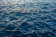 Dark Blue Sea Water With A Choppy  Texture And Reflected Orange Highlights From A Sunset