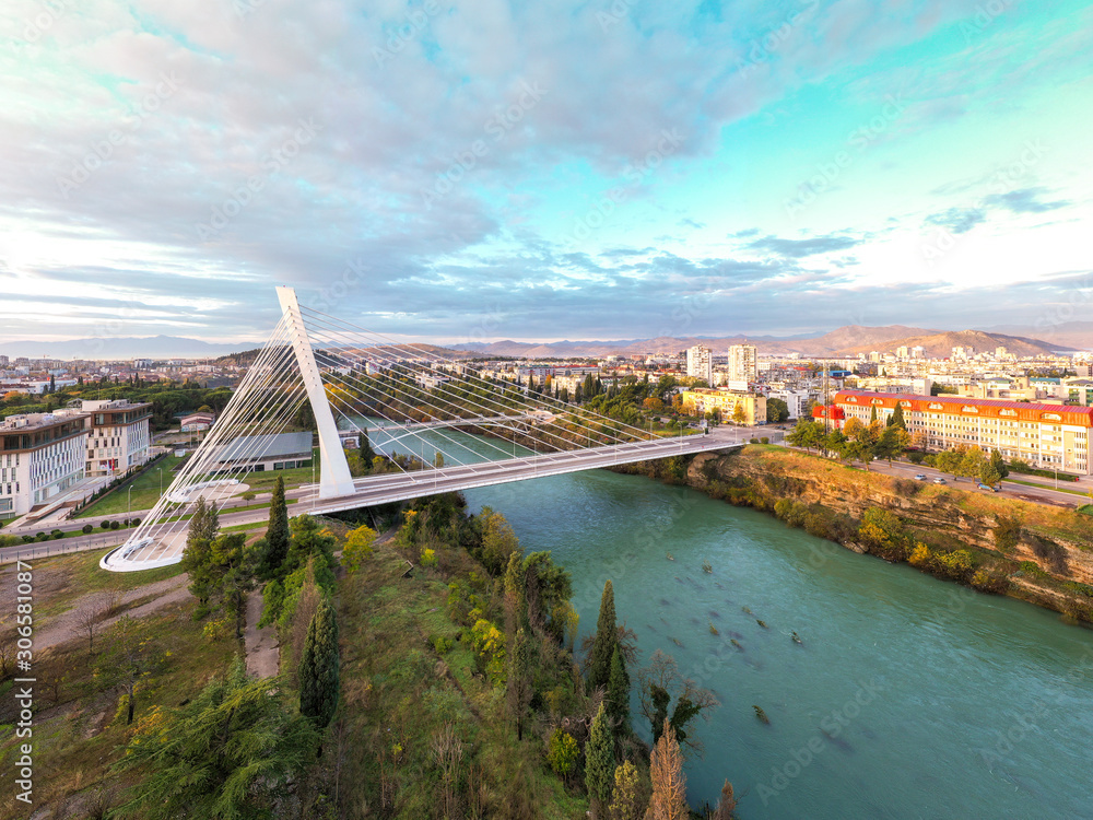 Obraz na płótnie Podgorica, Montenegro: aerial view of the city featuring Millennium bridge and Moraca river in the morning, at sunrise, under beautiful sky. Cable stayed bridge with green area in the foreground. w salonie