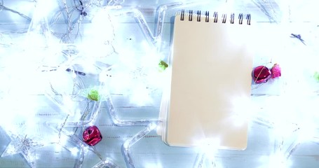 Wall Mural - Flat lay empty notepad with glowing Christmas stars and bells on wooden background. Shot in 4k resolution