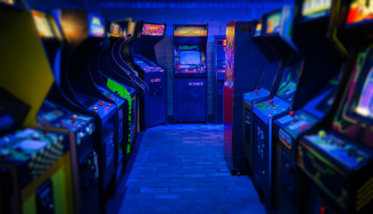 Old Vintage Arcade Video Games in an empty dark gaming room with blue light with glowing displays and beautiful retro design