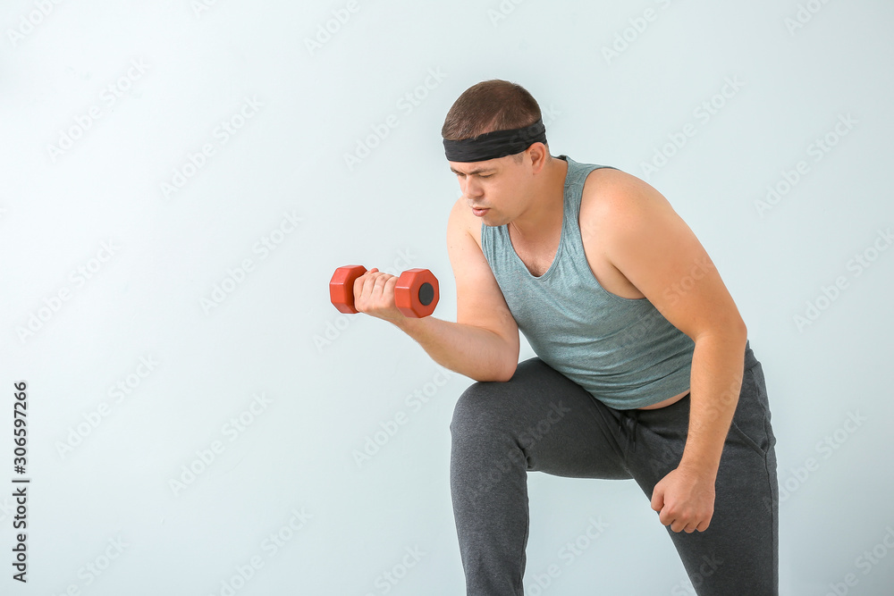 Overweight man with dumbbell on light background. Weight loss concept