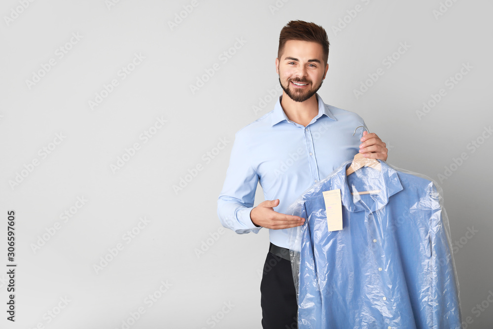 Male worker of modern dry-cleaner with clothes on light background