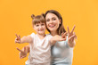 © Pixel-Shot - Portrait of happy mother and daughter showing victory gesture on color background