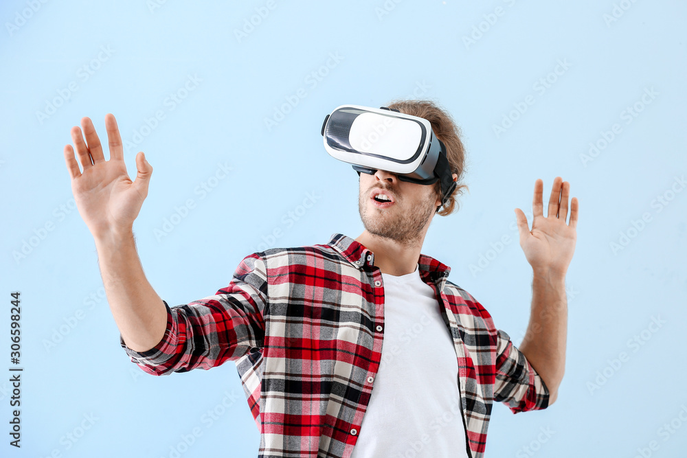 Young man with VR glasses on color background