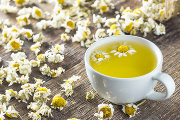 Wall Mural - white cup of chamomile tea with dry daisy flowers on rustic wooden background, herbal medicine hot drink concept