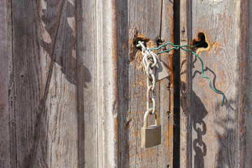 Two closed padlocks with a chain on an old wooden door