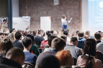 adult people at conference listen to woman speaker providing lecture on scene in big conference hall
