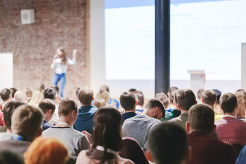 Adult people at conference listen to woman speaker providing lecture on scene in big conference hall. Business and Entrepreneurship concept. Audience at the conference hall.