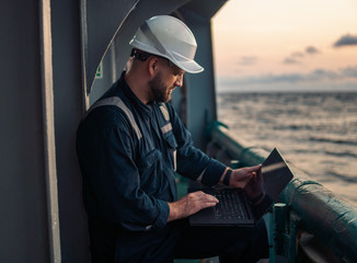 Marine chief officer or captain on deck of vessel or ship watching laptop. Internet and home connection at sea.