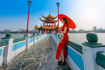 Wall Mural - Beautiful Asian Chinese Woman Wearing Cheongsam Traditional Red Dress standing on bridge at Wuliting pavilion,Kaohsiung,Taiwan.