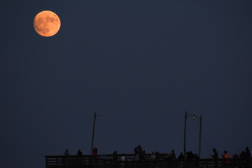 Moon rising on the horizon over a fishing pier on the beach