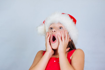 Wall Mural - little cute girl is standing in a Christmas hat and surprised at the holiday