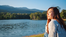 Portrait Image Of A Beautiful Asian Woman Sitting In Front Of The Lake And Mountains Before Sunset