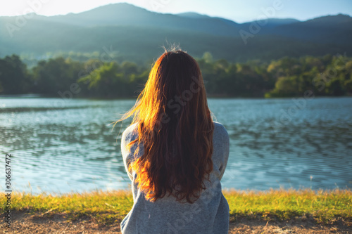 Fotomural A woman sitting alone by the lake looking at the mountains with green nature bac