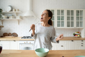 Happy woman singing in beater microphone dancing cooking in kitchen