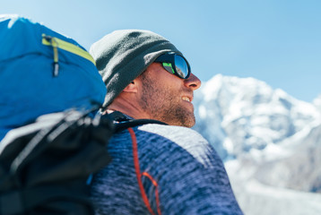 Portrait of unshaved Hiker man with backpack and UV protecting sunglasses on Taboche 6495m peakk background ,  He enjoying mountain views during Everest Base Camp trekking route.