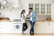 © fizkes - Romantic affectionate young couple drinking wine standing in modern kitchen