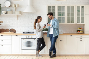 Wall Mural - Romantic affectionate young couple drinking wine standing in modern kitchen