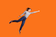 © khosrork - Superhero. Portrait of joyous pretty woman with brown hair in long sleeve shirt jumping high with one stretched arm, feeling to be superman flying up. indoor studio shot isolated on orange background