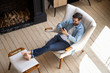 © fizkes - Relaxed guy sit on comfortable chair in house using phone