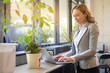 © Bojan - Mature businesswoman standing near windows and using laptop in modern office