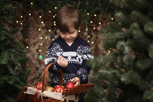 A Little Child By The New Year Tree. Children Decorate The Christmas Tree. Baby In A Sweater By A Green Tree In The Studio.