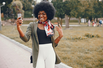 Wall Mural - Fashionable girl in a summer city. Black lady in a green jacket. Woman in a red scarf. Famale with mobile phone