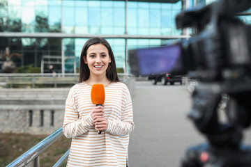 Canvas Print - Young female journalist with microphone working on city street