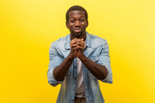 Portrait Of Hopeless Depressed Young Man In Denim Casual Shirt Holding Hands In Prayer, Pleading Asking Heartily, Looking With Guilty Expression. Indoor Studio Shot Isolated On Yellow Background