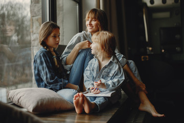 Wall Mural - Beautiful mother with two daughters. Family sitting in the room near window