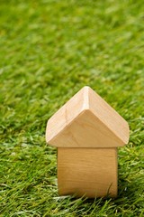 Wall Mural - Little wooden miniature house model on green grass background with copy space - ecological living or house building concept