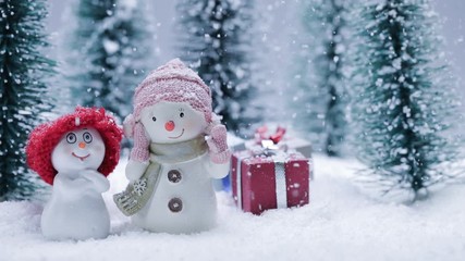 Wall Mural - Two small cute snowmen friends with gifts in forest under falling snow