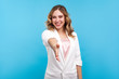 Welcome! Portrait of friendly hospitable cheerful woman with wavy hair in white jacket giving hand to handshake, hostess greeting guests, looking sociable positive. indoor studio shot, blue background