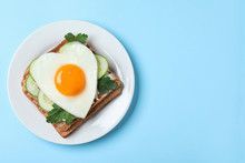 Plate Of Tasty Sandwich With Heart Shaped Fried Egg On Light Blue Background, Top View. Space For Text