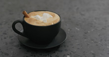 Cappuccino With Marshmallow And Cinnamon In Black Cup On Terrazzo Countertop
