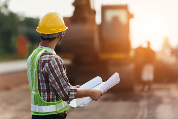 architect holding rolled up blueprints at construction site