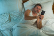 © TheVisualsYouNeed - domestic lifestyle high angle portrait of young attractive and relaxed man at home lying on bed wearing pajamas using mobile phone networking and looking social media